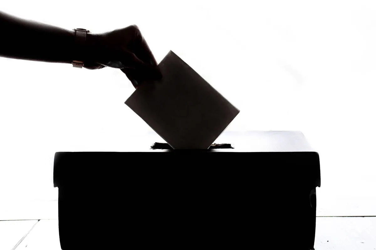 Silhouette of a hand placing a ballot paper into a ballot box